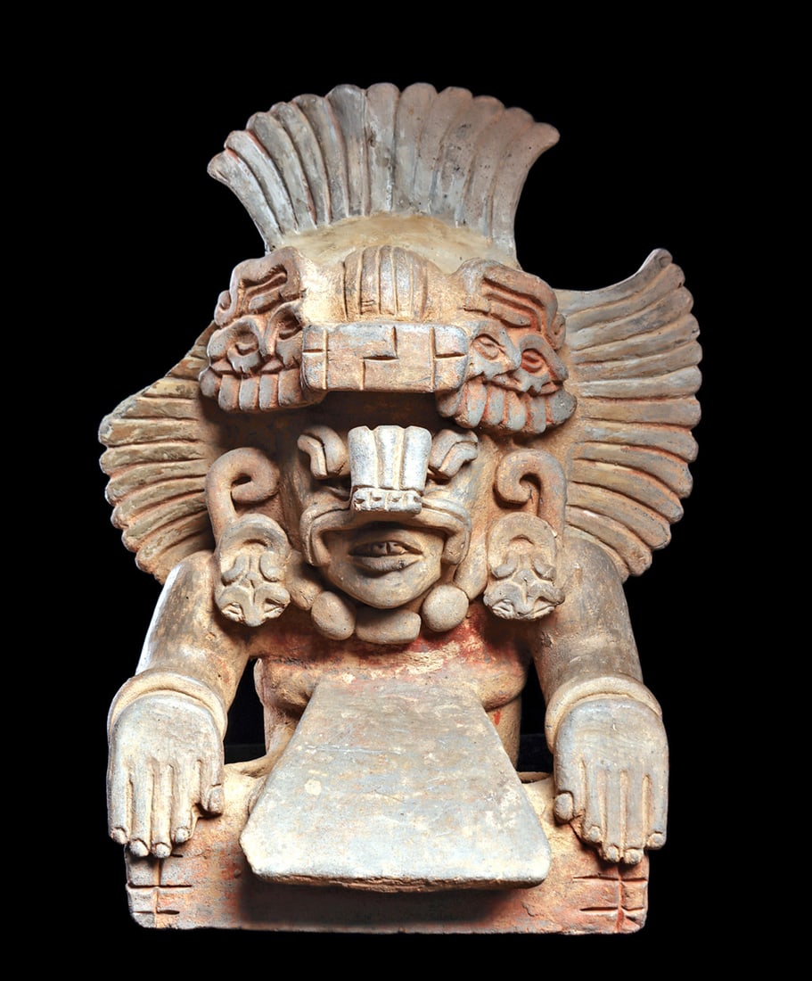 Zapotec Figural Urn with Buccal Mask: Large grayware pottery, figural urn, depicting a seated deity with crossed legs and hands resting on knees. Wearing a buccal mask, large beaded necklace and bracelets, fancy decorated ear spools, a la