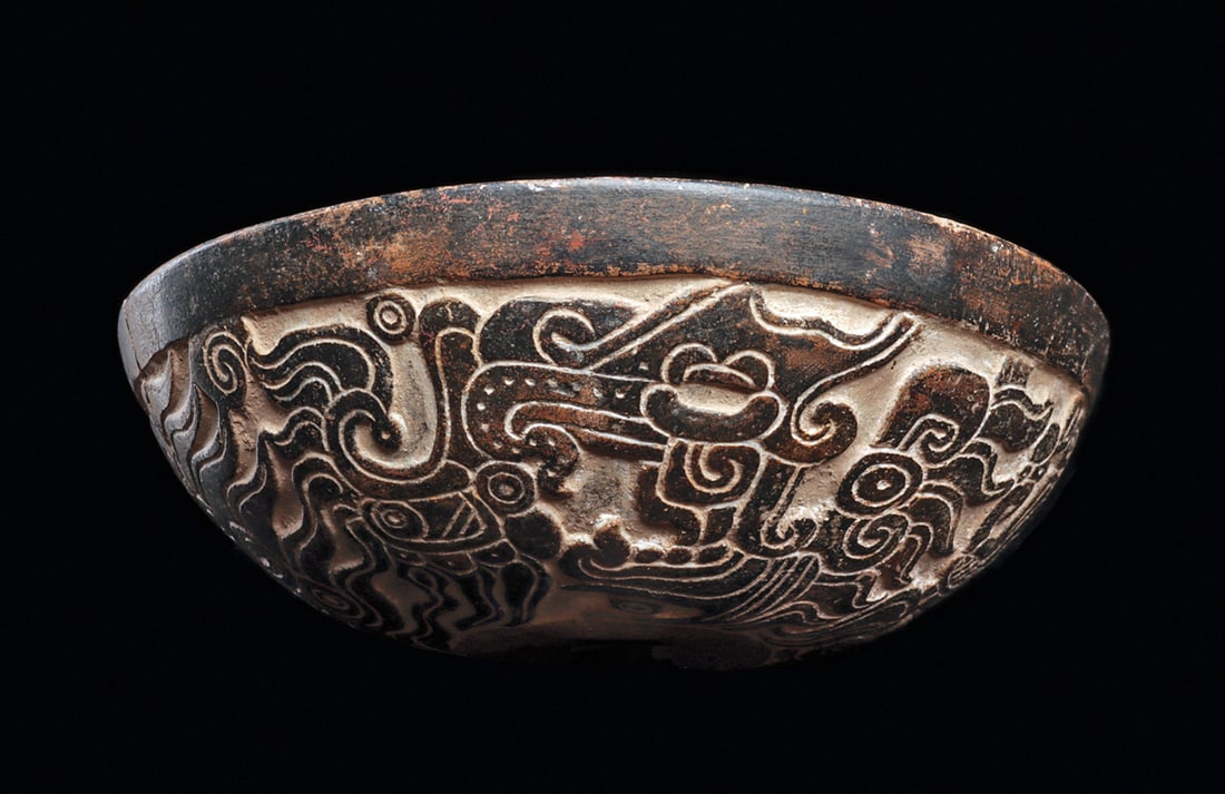 Veracruz Bowl with Carved Decoration: Fine pottery bowl having a deep relief carved decoration, with four large feline-like heads. Each has a large open fanged mouth, with flowing manes and emblems, painted on the exterior in black with a