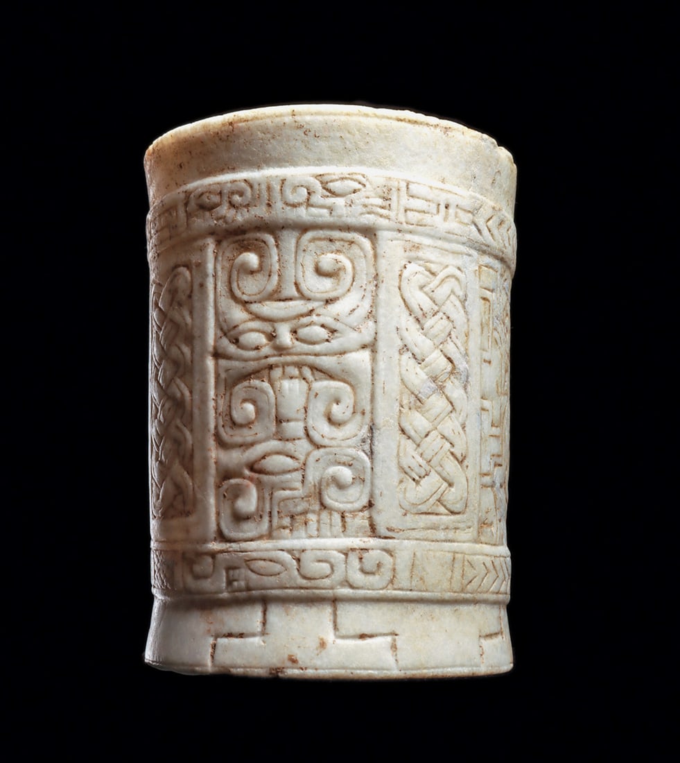 Classic Maya Marble Decorated Cylinder Vessel: White marble/calcite cylinder vase, relief carved on the exterior with relief upper and lower rim bands and a raised basal band. Carved repeat panels each containing a dancing monkey- like figure wear