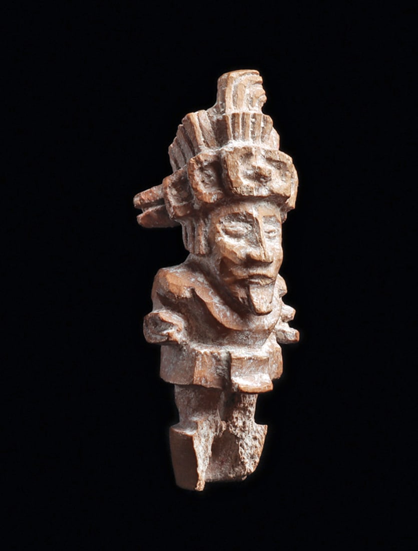 Maya Intricately Carved Miniature Bone Figural Finial: Fine carved miniature standing figural finial depicting a standing dignitary wearing a fancy feathered headdress with a stepped link headband. Beautifully carved facial features and wearing a goatee.