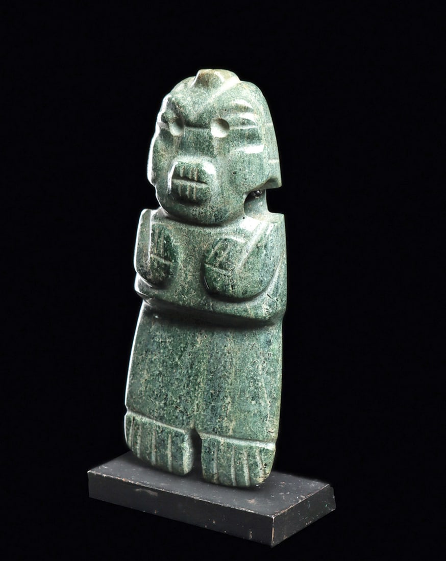 Costa Rican Axe God Figural Pendant: Carved blue-green jade anthropomorphic standing axe god figure, holding both of his arms over his chest. Relief carved facial features, oval toothy mouth, squared shoulders, arched brows, drilled roun