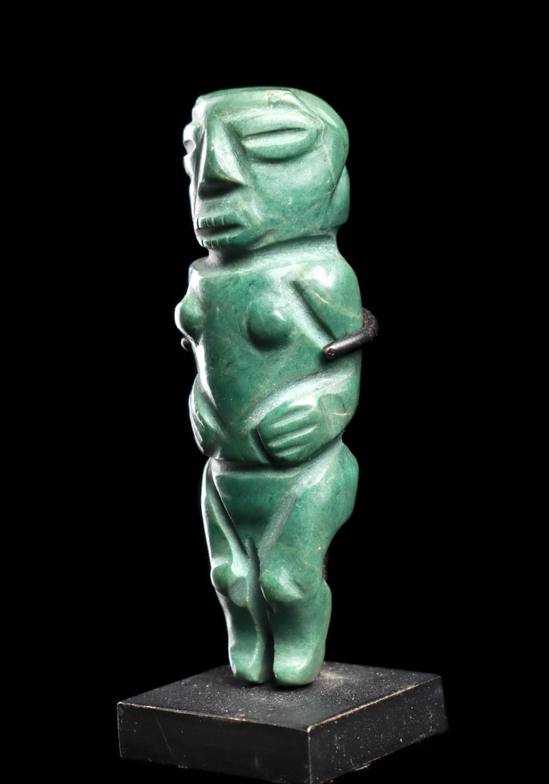 Costa Rican Jadeite Figural Pendant: Carved blue-green jadeite stone anthropomorphic pendant depicting a standing female figure, holding both of her hands on her stomach. Small round breasts and round knee caps, relief carved facial feat