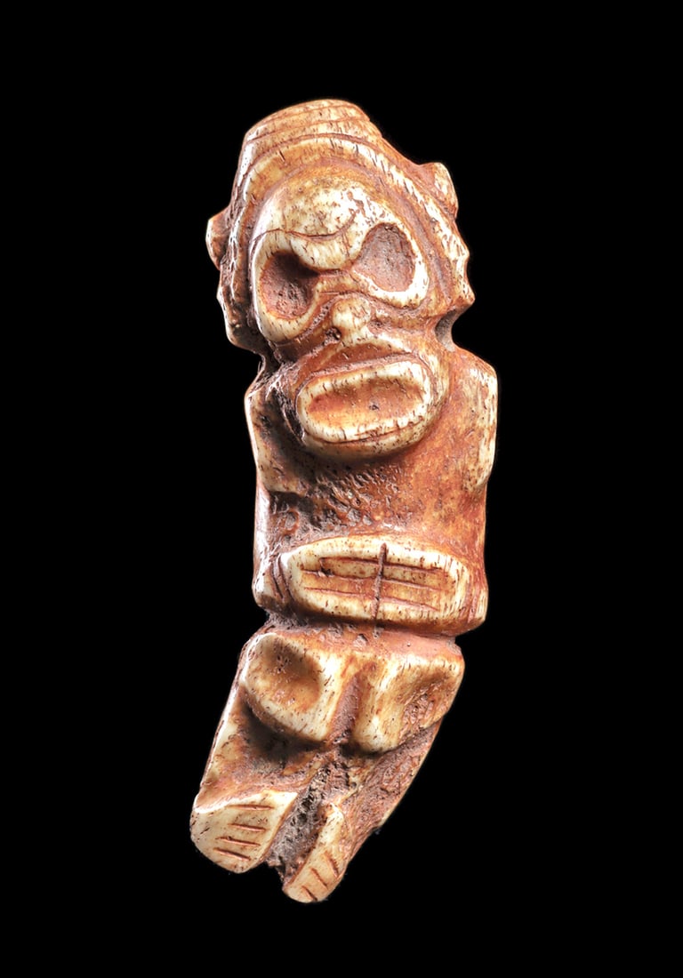 Taino Bone Figural Pendant: Carved bone figural pendant depicting a standing stylized human figure with a curved body, which was carved along the natural curve of the probable rib bone. He holds both hands over his stomach, feet