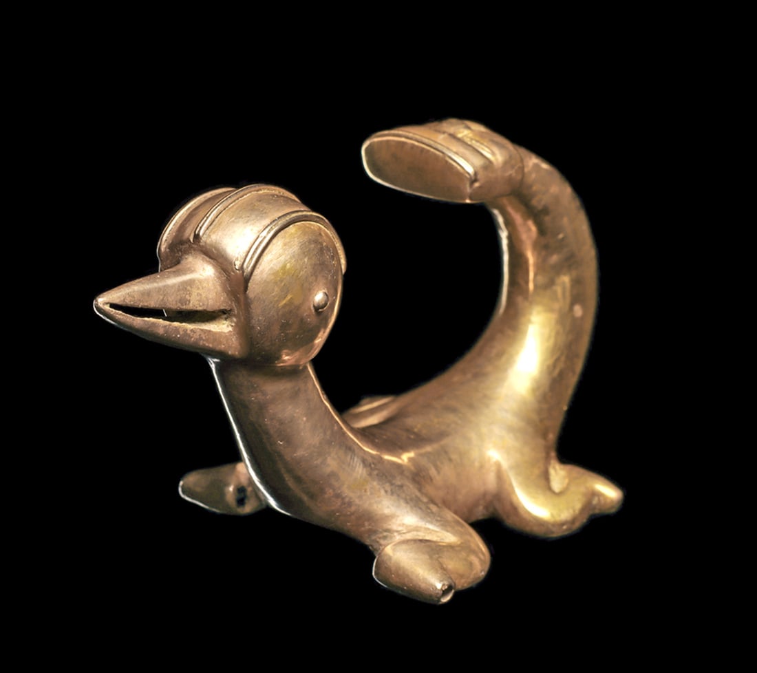 International Gold Curly-Tailed Animal with Human Head: Fine and large gold figural pendant depicting a curly-tail lizard with a large round avian head, having a long pointed beak, and a low triple head crest. A stylized human head is at the tip of his tai