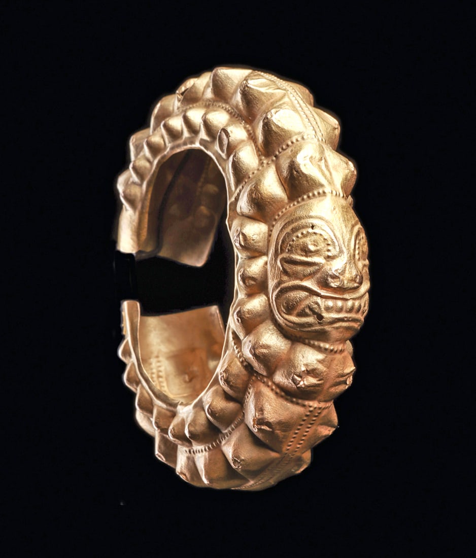 Ecuadorian Large Gold Ear Ornament: Large high relief decorated hammer molded sheet gold ear ornament, made to fit over and surrounding the ear. Depicted with a deity head in the center having expressive facial features and a wide fange