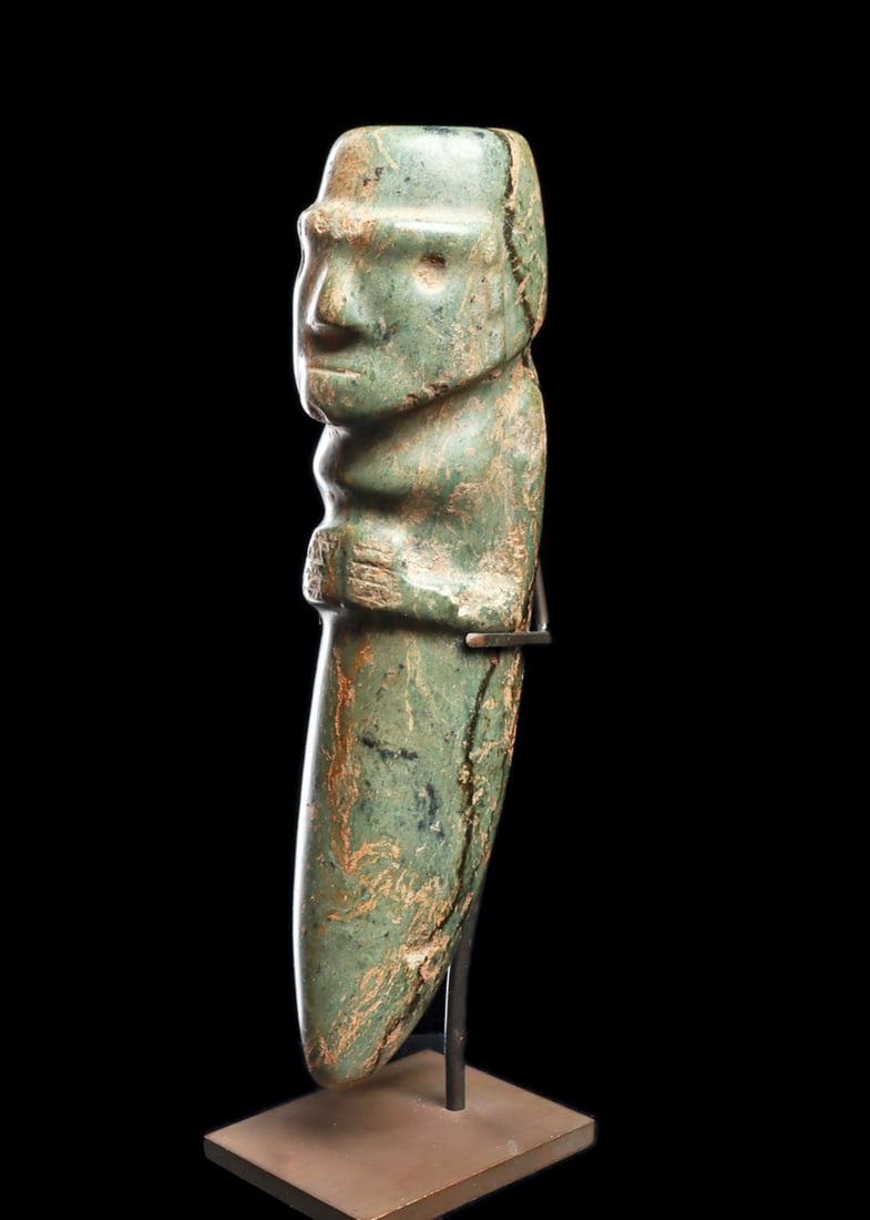 Ecuadorian Serpentine Figure with Tapered Base: Carved verigated blue-green stone anthropomorphic votive figure, holding both hands to his stomach, with delineated fingers. Strong jaw and browline, relief carved facial features, small round drilled