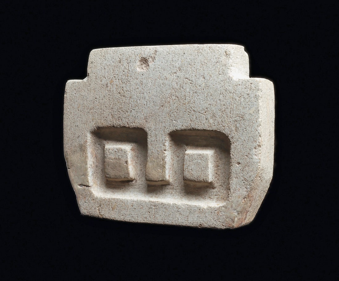 Valdivia Limestone Slab Head: carved compacted limestone votive head of angular stepped form, with deeply carved square eyes with raised pupils. A few small restored surface and edge chips, otherwise intact. old metal base. 3-1/2"