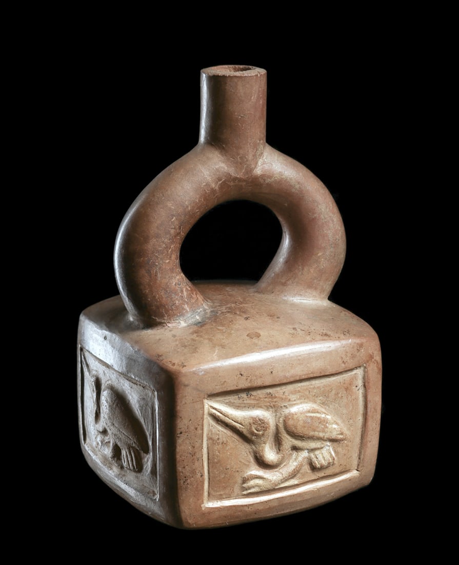 Moche Cube-Bodied Vessel with Birds: Pinkish-cream pottery cube-bodied bottle having a stirrup type spout. Body is decorated with four recessed rectangular panels, each having a crouching seabird with a long beak. Tip of chimney spout is