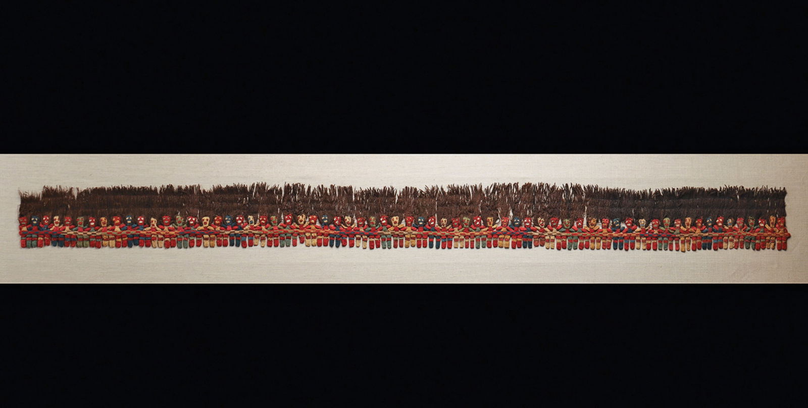 Proto-Nazca Muneka Border Fringe: Classic alpaca fiber, single needle knit border composed of sixty-five figures or dolls whose hair is the fringe of the mantle. This colorful example has dramatic expressions on the faces of the figur