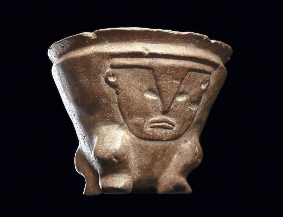 Argentinean Stone Figural Kero: Carved gray-brown stone kero of conical form and decorated on both sides in relief with two opposing kneeling human figures. Different large faces, wearing head bands and small ear spools, their legs