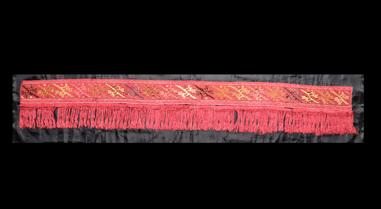 Chancay Textile Fringed Border: Tightly woven multicolor textile border having long red string fringes connected to a wide border panel having a wide center band decorated with nineteen pairs of felines standing on a central stepped