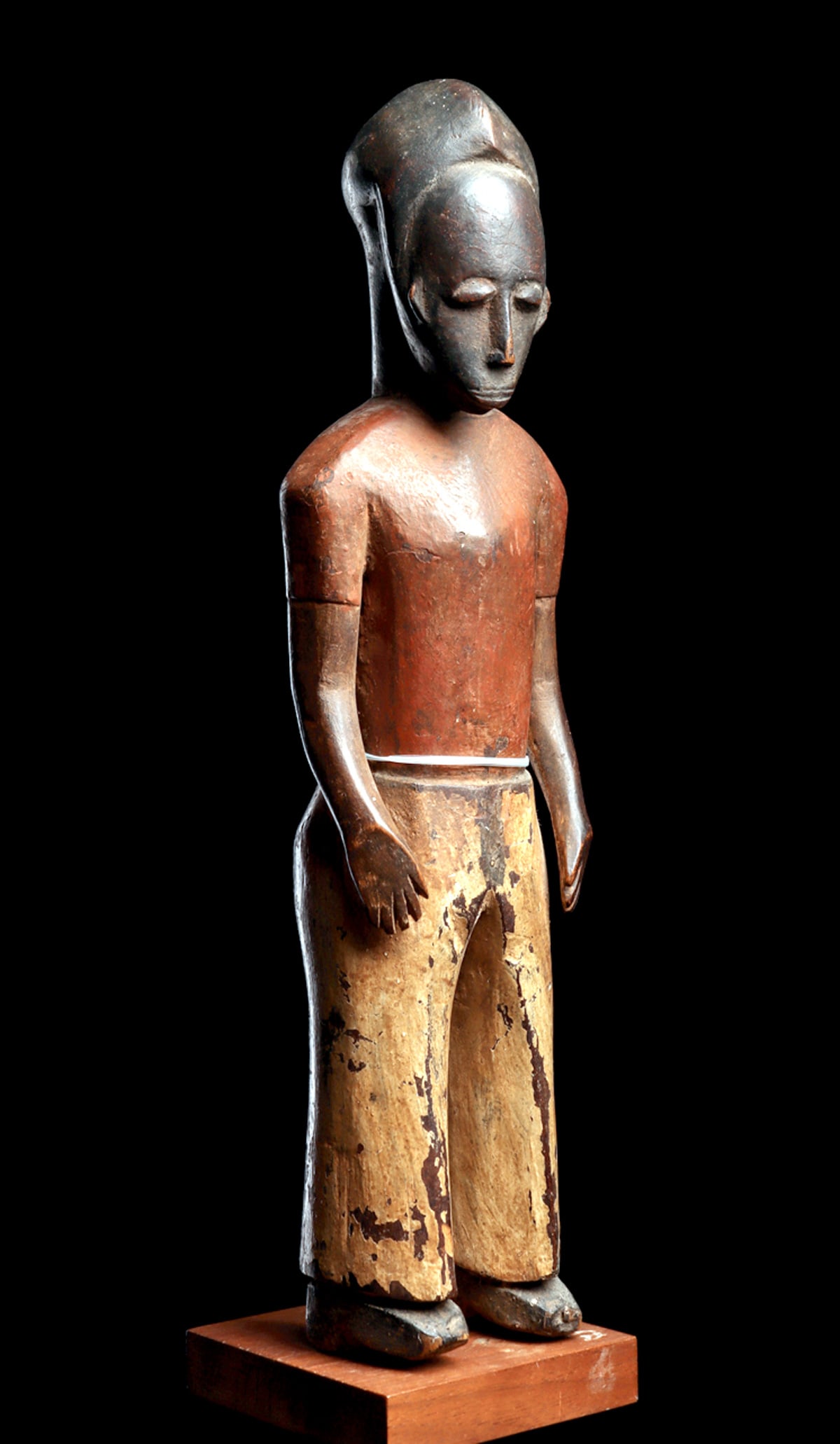 Baule Colonial Figure: Male figure wearing heeled boots, pants and short sleeve shirt, having tranquil expression with downcast eyes, high forehead, and tapered crest hairdo. Surface wear, minor paint loss. Custom base.