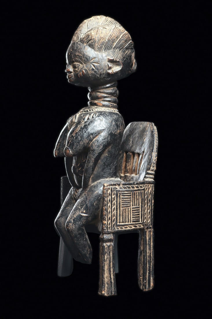 Mende Figure: Rare Mende sculpture depicting a broad-bodied female figure seated on a high-backed chair, richly carved and powerfully present with regal expression. She is adorned with an elaborate plaited coiffure