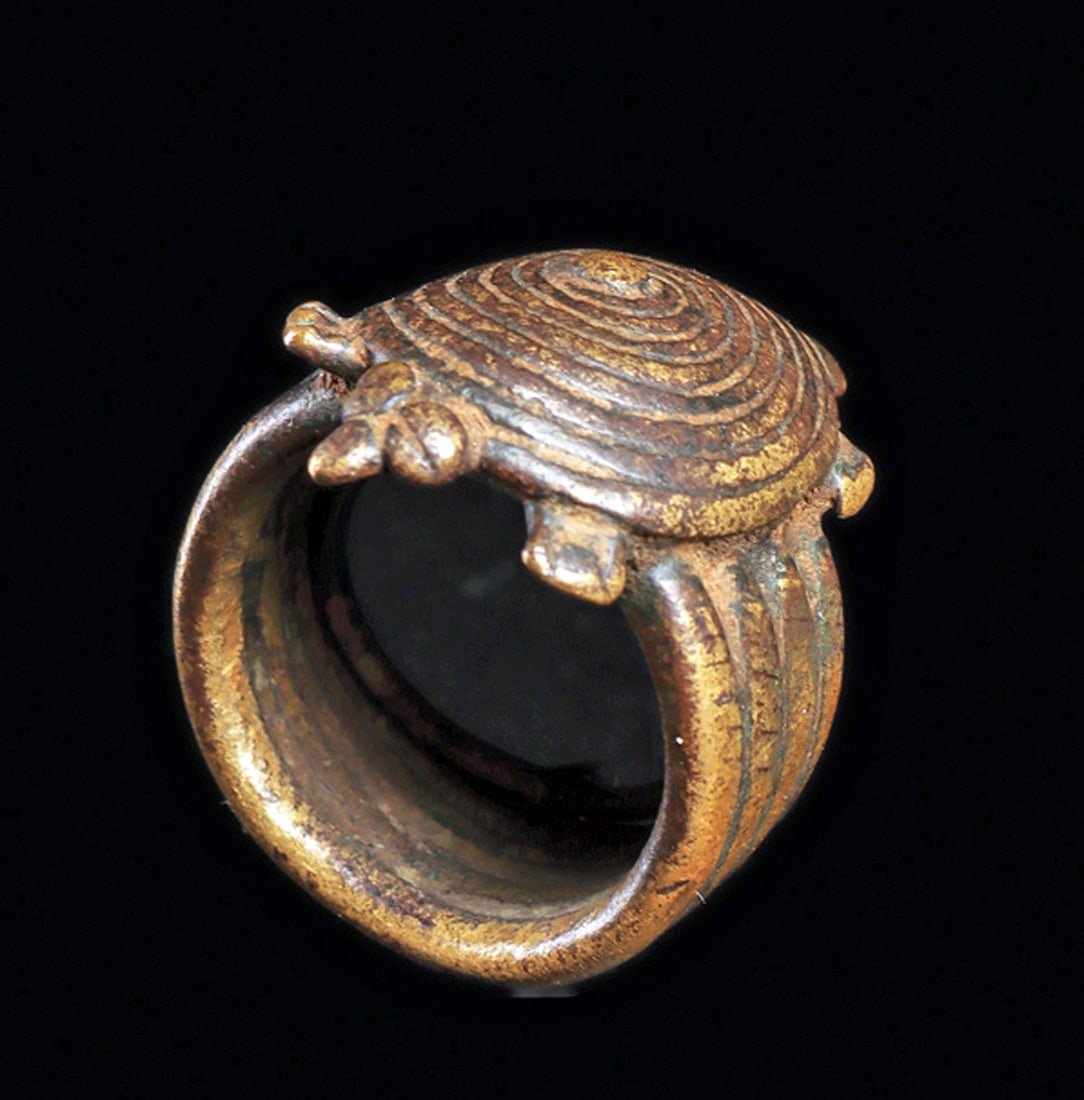 Published Bronze Turtle Ring: Copper alloy ring identified by Wheelock in his publication as Tusyan, the band composed of four rings, and a circular shell body turtle with tiny head, paws and tail. Worn patina. Custom base. 1"H. f