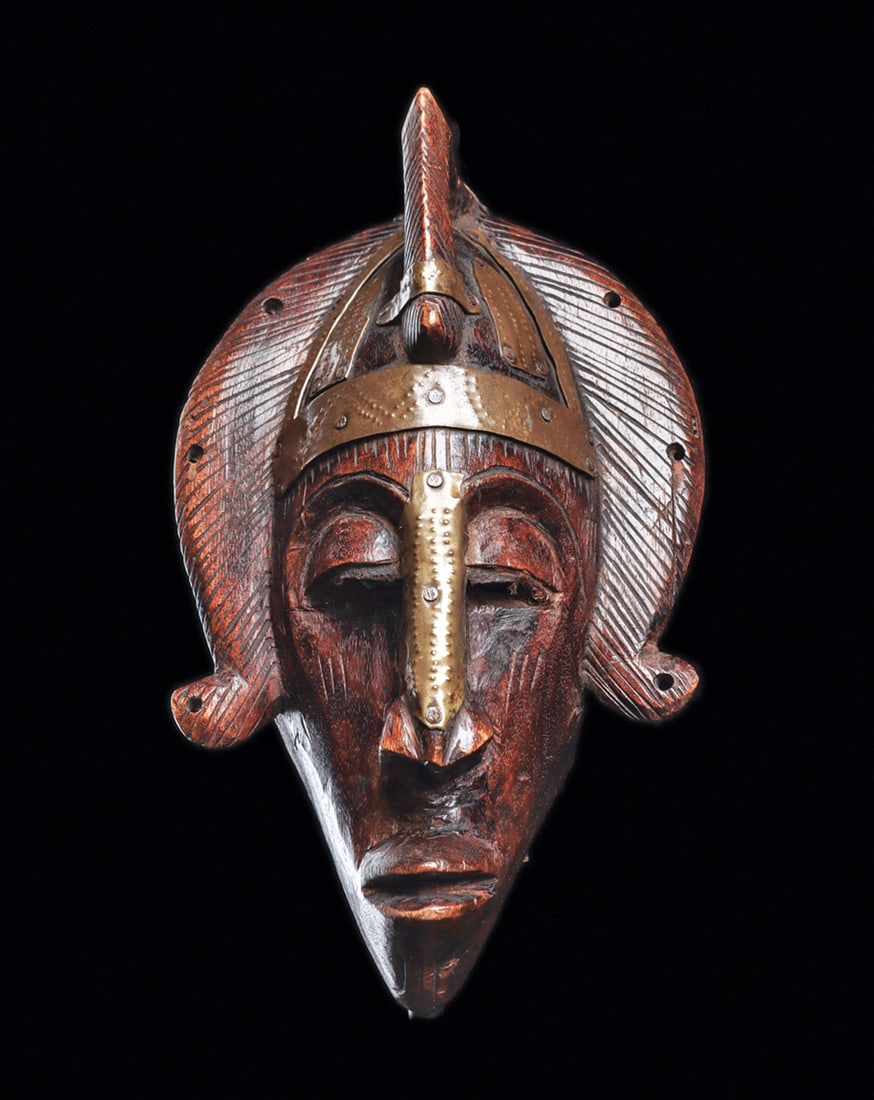 Marka Female Mask: Carved wood mask known as "Dyoboli Koun", with curved hair tresses on sides and angular extension at top of forehead, with brass alloy strips with pinprick detail. Dark brown burnished patina with wax