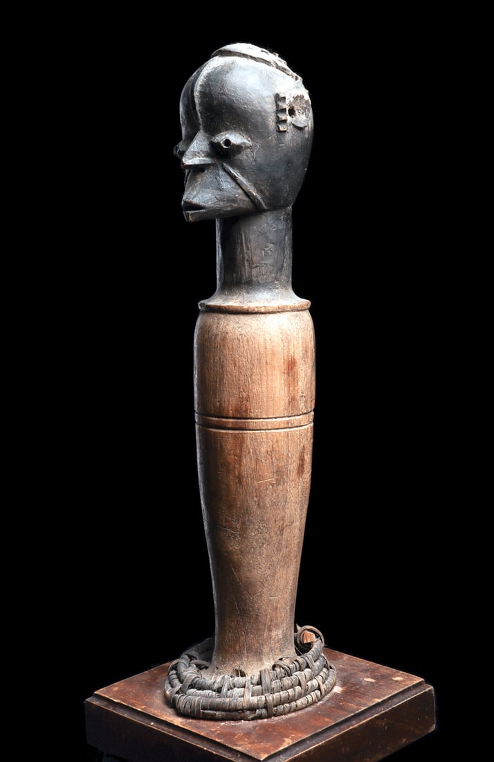 Idoma Dance Crest Figure: Carved wooden head crest of elongated cylindrical form, surmounted by an ancestral head with bulging eyes, a coiffure articulated with inserted plugs, pronounced relief scarification, and a projecting