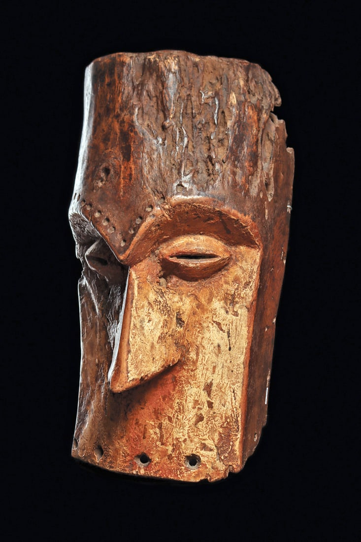 Large Lega Mask: Massive Bwami society wood mask of distinctive minimalist form, with tall burnished forehead, forming aggressive overhanging brow lined with concavities. The inset face with large relief lentoid eyes,