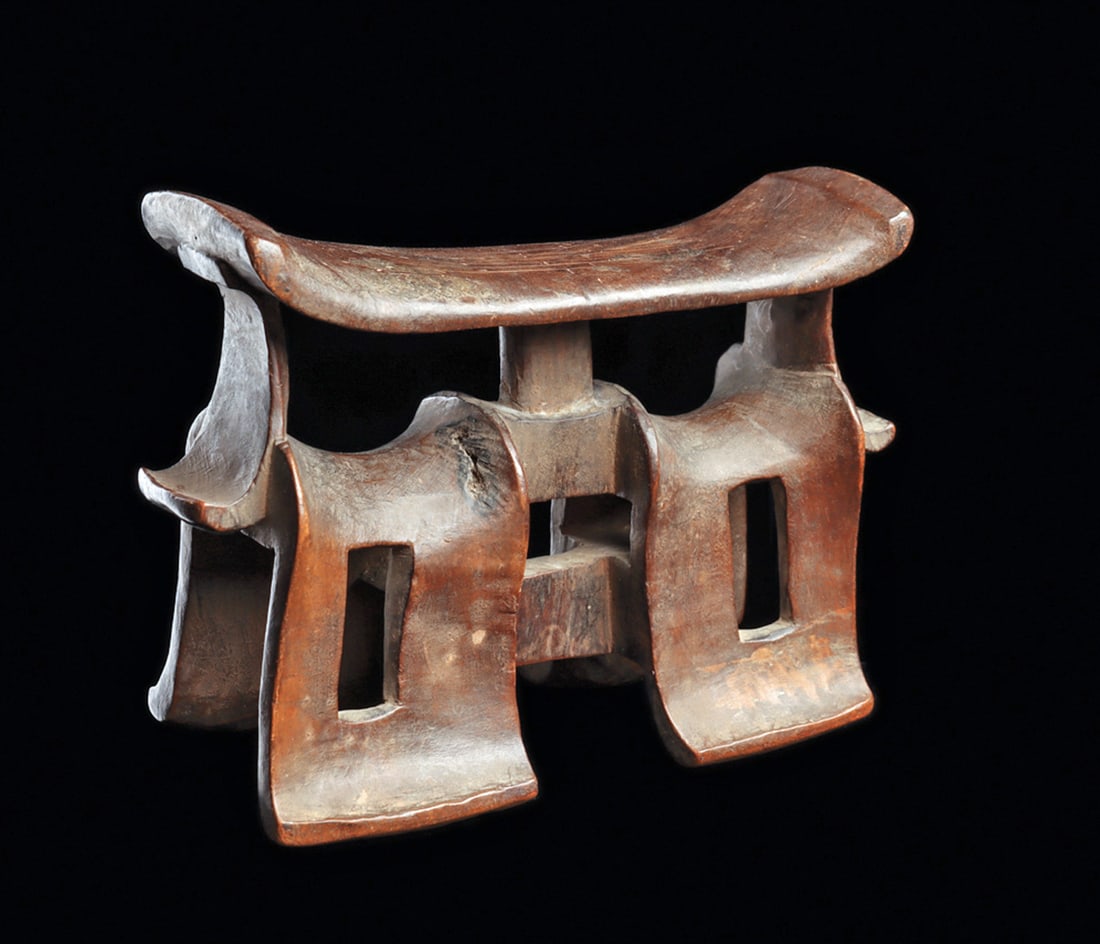 Tsonga Neckrest: Carved wood neckrest "chidani / xhinkenhela" on two openwork saddle-shape legs supporting a rectangular pillow with curved ends. One corner of pillow chipped. Medium red-brown patina. 5"H. x 6-1/2"L.