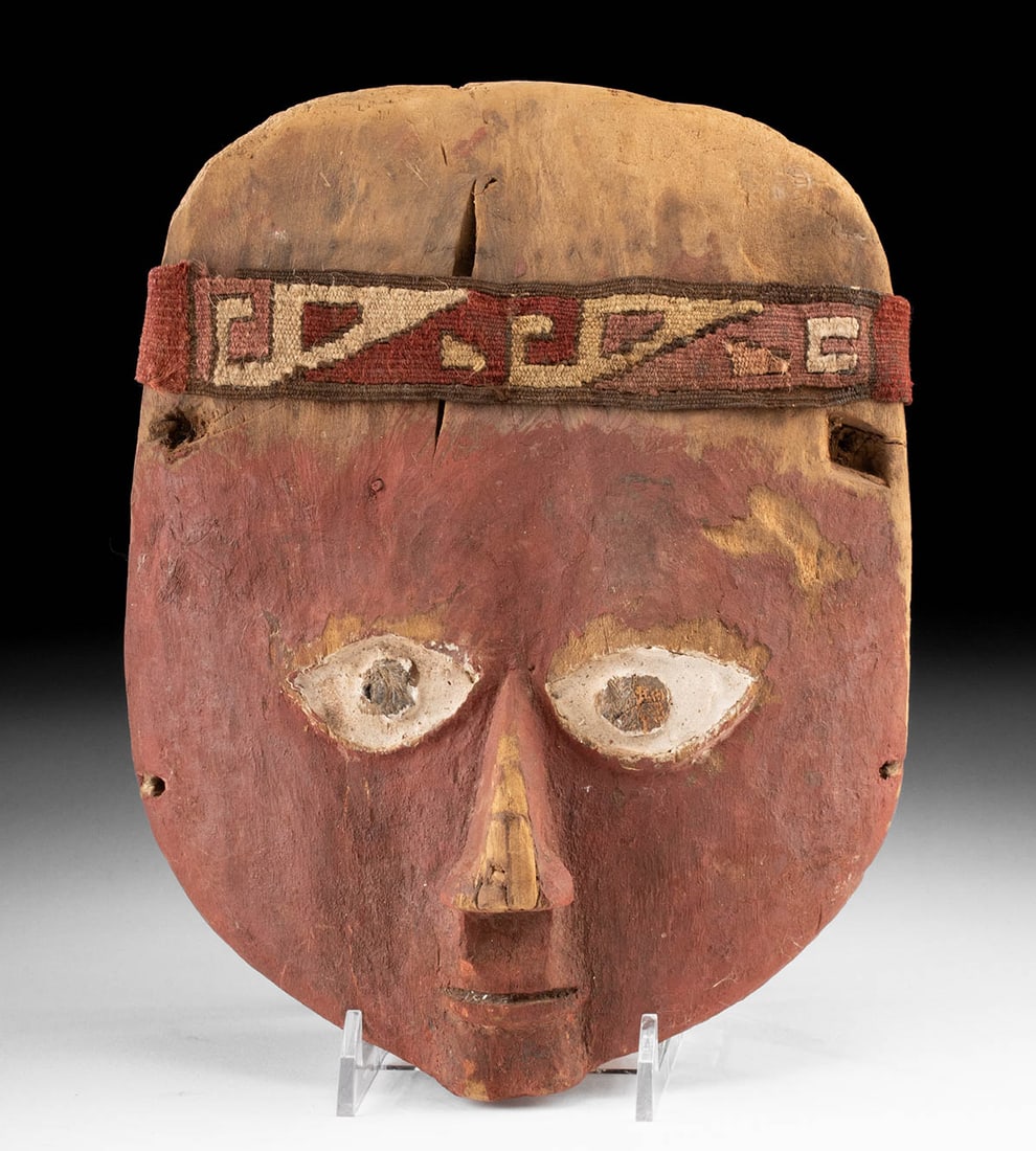 Chancay Mummy Bundle Mask - Red Pigment. Textile Band: Pre-Columbian, Central Coast Peru, Chancay, ca. 1000 to 1425 CE. A large funerary mask carved from wood, painted with red cinnabar pigments, and adorned with a finely hand-woven textile headband made