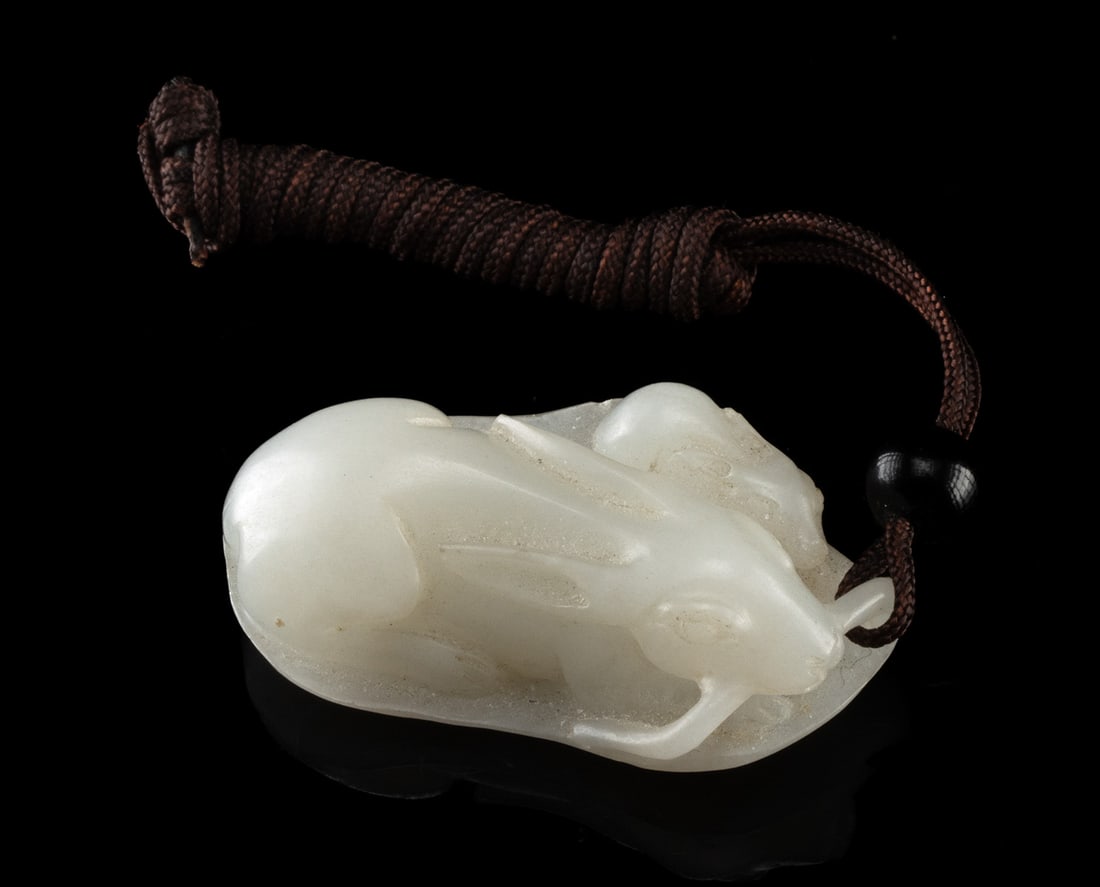 Japanese Mother & Baby Rabbit Jade Netsuke: East Asia, Japan, ca. early to mid-20th century CE. A carved white jade netsuke depicting a mother rabbit resting protectively with her baby upon a broad, gently veined leaf, the stem delicately held
