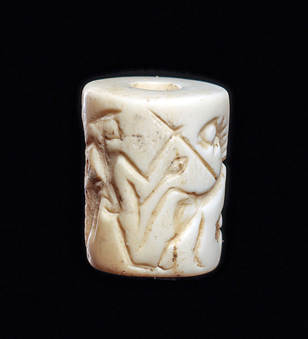 Early Dynastic White Marble Cylinder Seal Battling Lion: Carved white marble cylinder seal having a carved rollout impression depicting a man spearing a lion flanked by another standing figure with spear. A large ancient surface chip between the scene, othe
