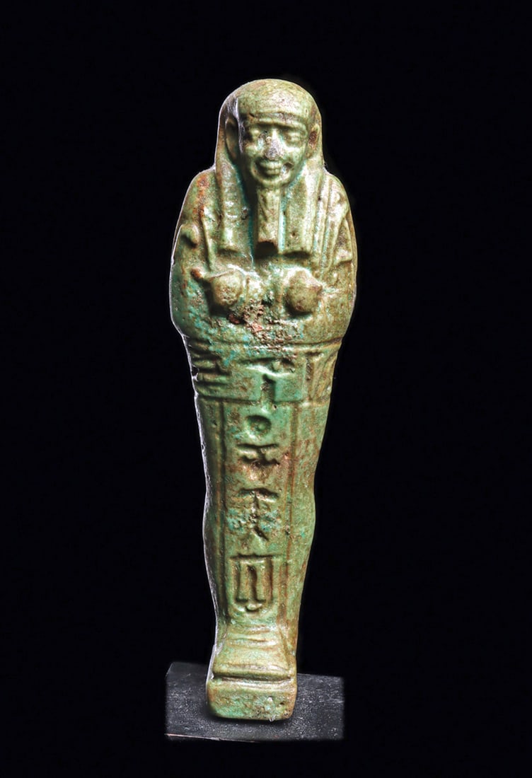 Egyptian Green Faience Ushabti: Small molded green glazed faience pottery mummiform ushabti depicted wearing the royal wig and beard, holding implements in both hands. Horizontal glyph band around his waist with a vertical glyph ban