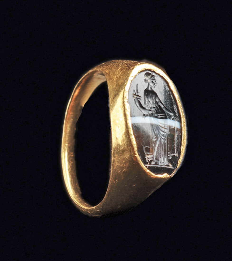 Roman Gold & Banded Agate Finger Ring: Gold finger ring having a rounded tapered shank with a wide oval bezel set with a long oval banded agate intaglio carved with the figure of the standing Fortuna holding a cornucopia, wearing a floor l