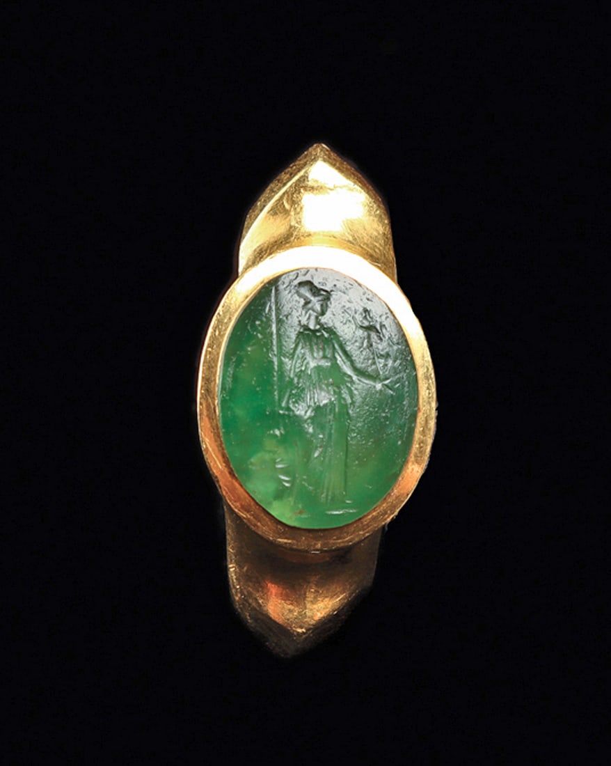 Roman Gold Ring with Intaglio of Minerva: Gold finger ring having a tapered gold shank with a raised center rib and notched shoulder, oval bezel set with an emerald-green glass cabochon which is engraved with a depiction of Minerva holding a