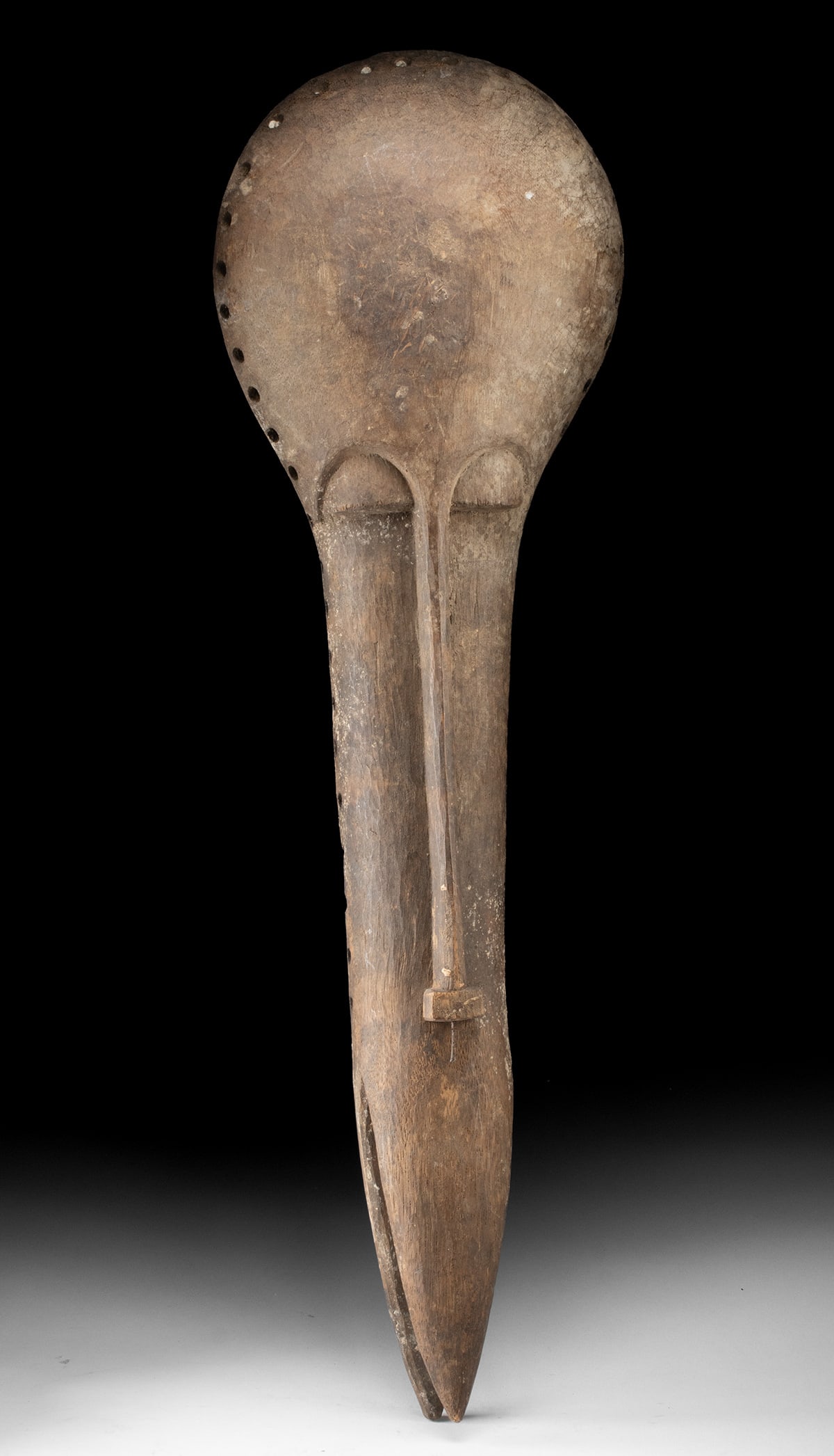 Mali Bamana Tribal Elongated Wood Mask: West Africa, Mali, Bamana (Bambara) culture, ca. 19th to early 20th century CE. A carved wood mask presenting a highly abstracted, elongated face with a smooth, rounded cranium and attenuated lower se