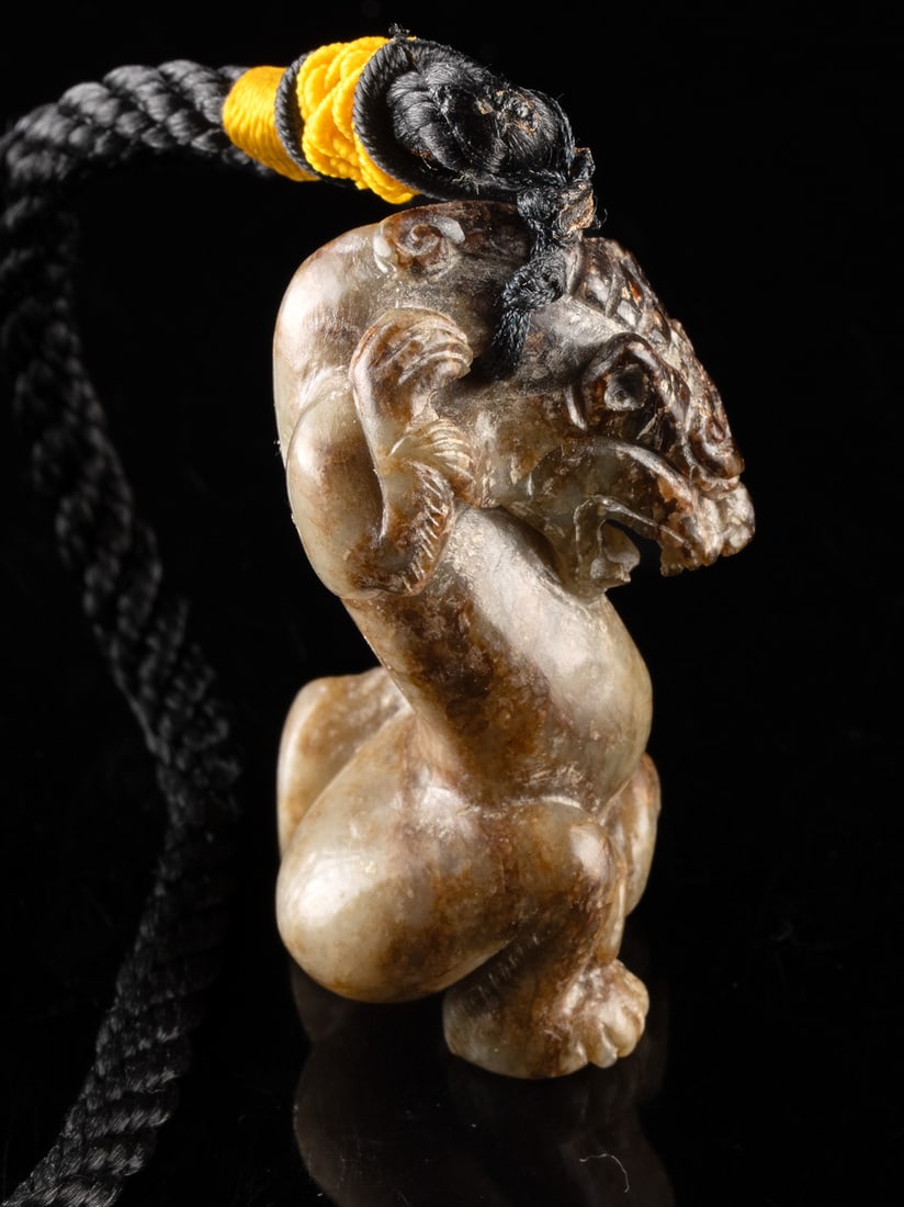 Chinese Serpentine Pixiu / Tiger Talisman: East Asia, China, ca. 20th century CE. A carved serpentine figure depicting a pixiu or stylized tiger, shown in a kneeling posture with arched back and expressive features. A black nylon cord with a y