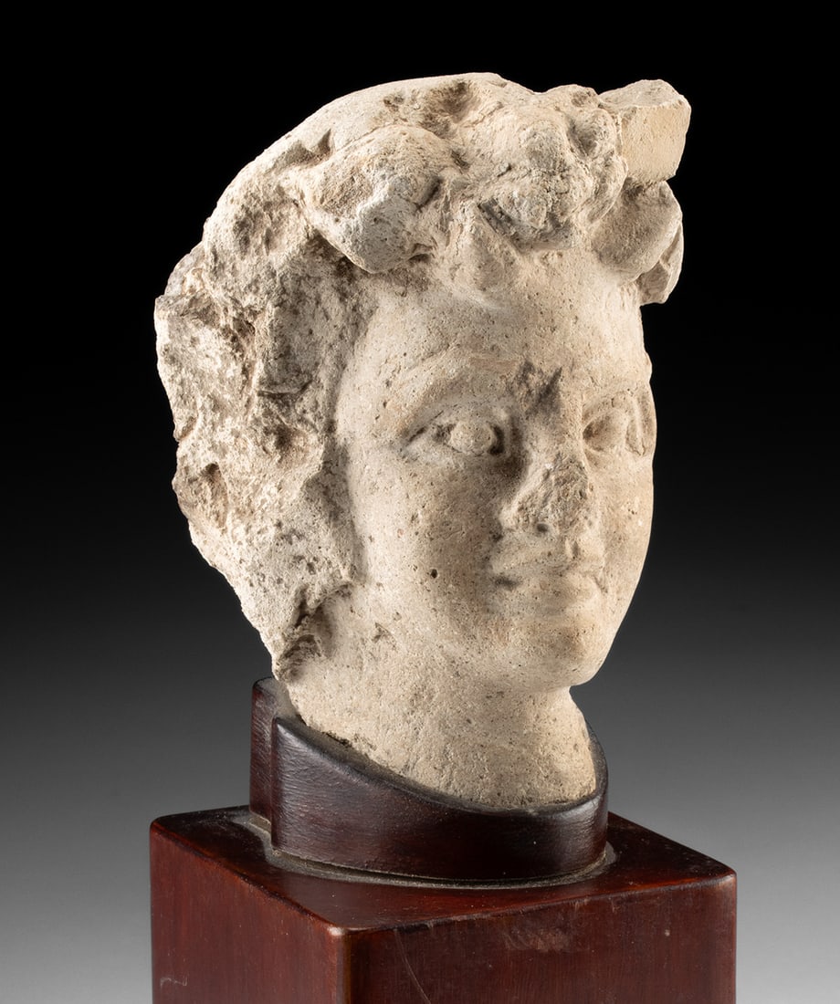 Gandharan Stucco Head of a Youth, Possibly Cupid: Ancient Central Asia, Gandhara, Kushan period, ca. 2nd to 4th century CE. A softly modeled head emerges from time with the quiet charm of youth, its features poised between classical ideal and devotio