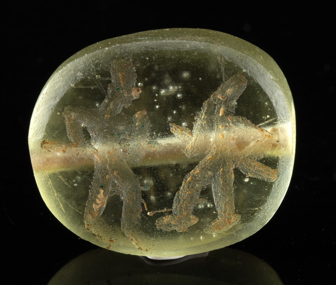 Sasanian Glass Stamp Seal with Warrior Combat: Ancient Near East, Persia, Sasanian period, ca. 3rd to 7th century CE. A translucent pale green glass stamp seal bead or amulet from the Sasanian period, engraved with a dynamic scene of two warrior f