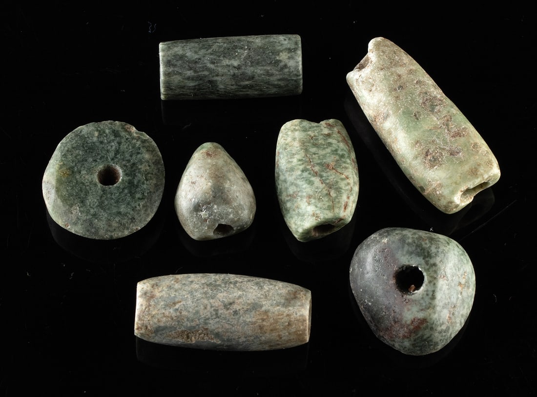 Mezcala-Maya Greenstone & Jadeite Bead Collection: Pre-Columbian, Southern Mexico, Mezcala to Maya culture, ca. 600 BCE to 900 CE. A group of seven hand-carved greenstone and jadeite beads. The beads display a range of compact forms, including barrel,
