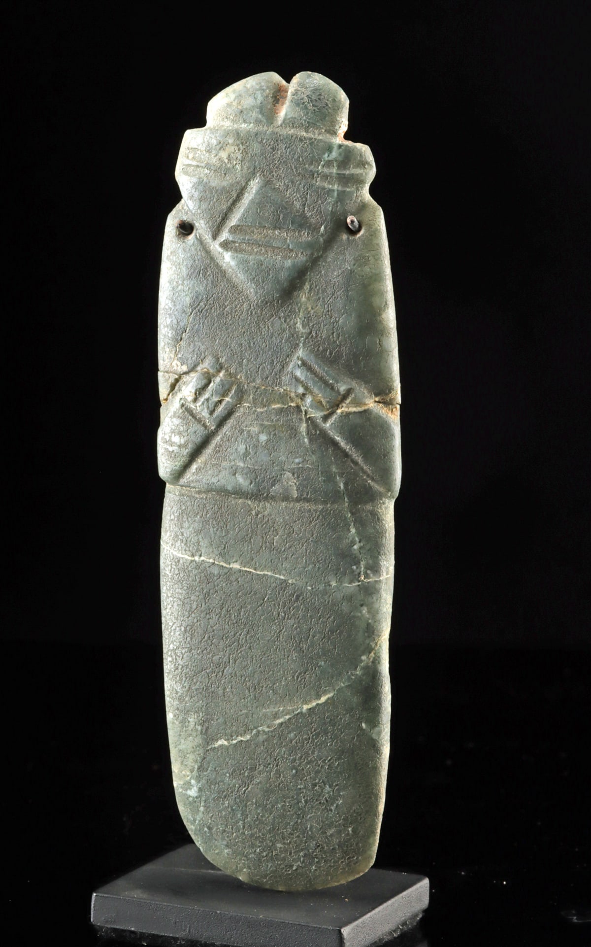 Costa Rican Nicoya Greenstone Figural Celt Pendant: Pre-Columbian, Central America, Costa Rica, Nicoya, ca. 700 to 900 CE. A quietly arresting Nicoya greenstone pendant shaped as a figural celt, this sculpture carries the cool green of ancient stone