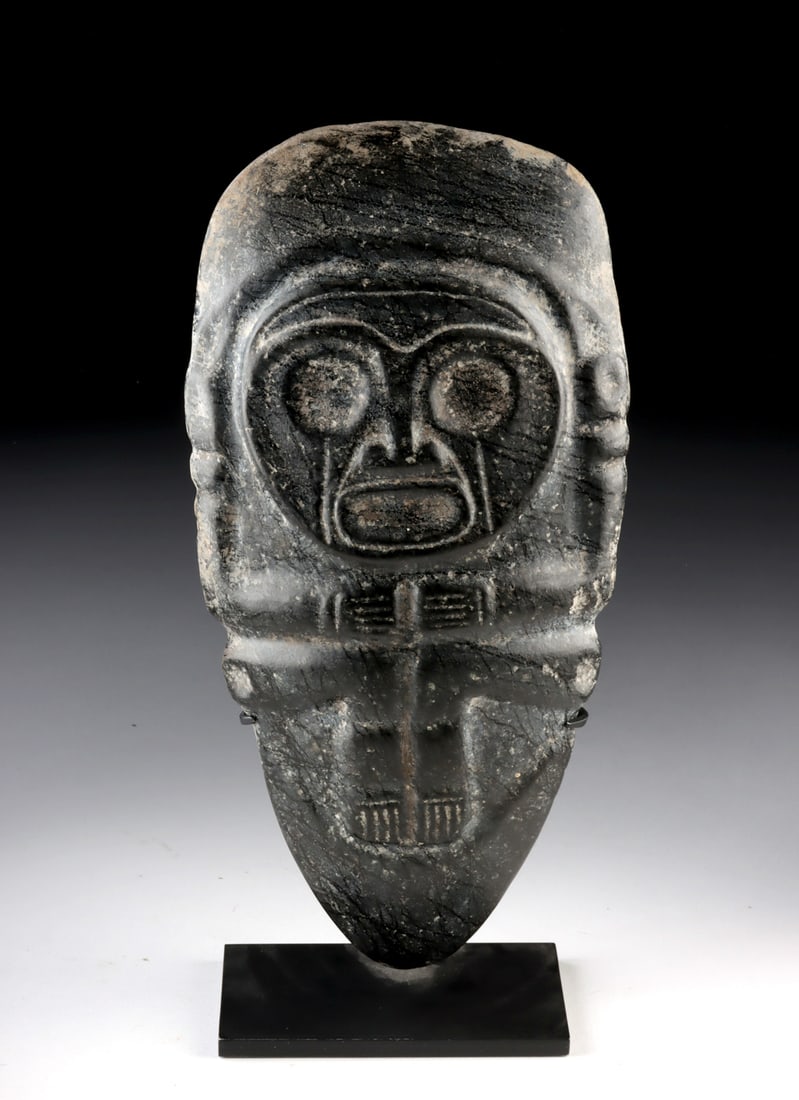 Taino Black Stone Zemi Figure Idol: Pre-Columbian, Caribbean, Taino, ca. 1000 to 1500 CE. A carved stone zemi figure formed from dense dark stone, the surface worked into an abstract anthropomorphic form with large circular eyes, a