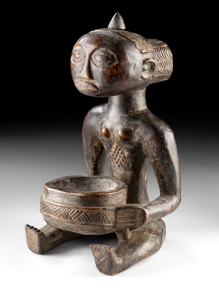 19th C. Luba Female Bowl Bearing Figure - Mboko: Central Africa, Democratic Republic of the Congo, Luba, ca. 19th to early 20th century CE. A dignified Luba mboko figure sits poised in quiet authority, her elongated form presenting a carved bowl