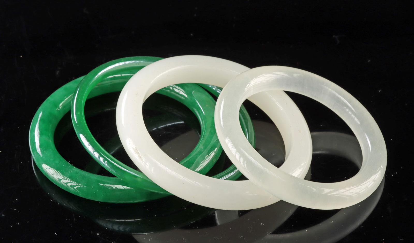 4 Chinese White Stone & Green Glass Bangle Bracelets: East Asia, China, ca. mid-20th century CE. A collection of four bangle bracelets including two carved from pale white stone with soft translucent surfaces and two formed from vibrant green glass. The