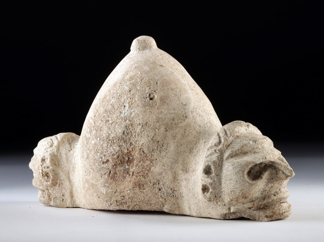 Taino Fossilized Coral Trigonolith w/ Twin Zemi Heads: Pre-Columbian, Caribbean, Taino culture, ca. 1200 to 1500 CE. A compelling Taino trigonolith carved from fossilized coral, its dense, porous surface preserving the natural texture of ancient marine li