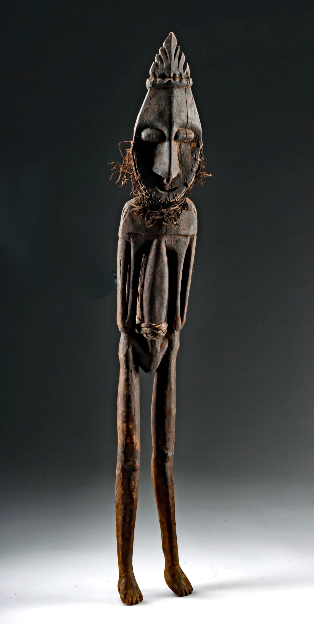 Papua New Guinea Sepik River Wood Ancestral Figure: Oceania, Papua New Guinea, Sepik River region, ca. early to mid-20th century CE. A slender carved wooden ancestral figure with elongated limbs, a plaited cane waistband, and raffia fiber tassels attac