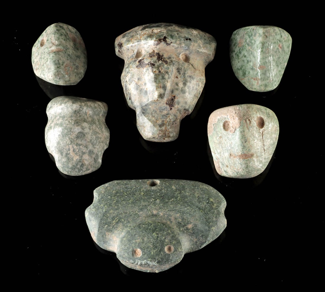 Lot of 6 Guerrero Mezcala Greenstone Head Amulets: Pre-Columbian, Mexico, Guerrero, Mezcala culture, ca. 700 to 200 BCE. A compelling group of six Mezcala greenstone pendants or beads carved in the form of abstract human heads, their simplified
