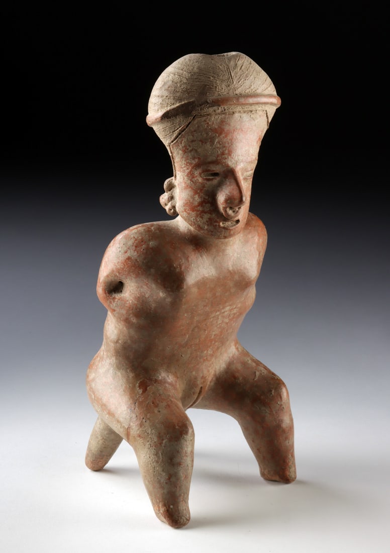 Jalisco Shaft Tomb Pottery Seated Nude Female Figure: Pre-Columbian, West Mexico, Jalisco, ca. 300 BCE to 300 CE. A hand-built and burnished pottery female figure shown seated nude, the bent legs forming a tripod support with two rear projections. The bo