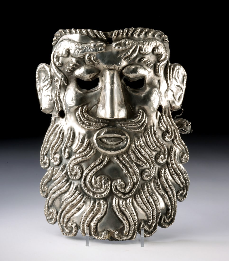 Mexican Guerrero Silver Mask w/ Lizard Motif Bell: Latin America, Mexico, Guerrero, ca. mid-20th century CE. A commanding silver visage confronts the viewer, its luxuriant beard unfurling in rhythmic curls while two lizards meet in silent tension acro