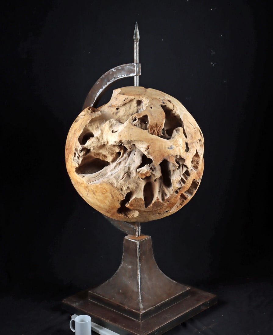 Monumental Teak Wood Globe on Steel Axis, ex-Tremonti: Southeast Asia, Indonesia, ca. late 20th to early 21st century CE. A monumental carved teak root sphere, formed from a single dense burl, displaying dramatic natural voids, tunnels, and organic contou