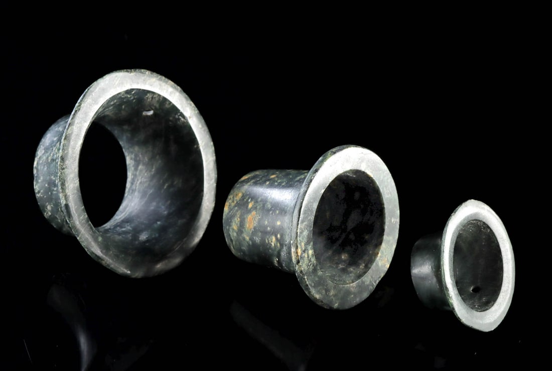 Group of 3 Classic Maya Stone Earspools: Pre-Columbian, Mesoamerica, Maya, Classic period, ca. 250 to 900 CE. A refined trio of carved stone earspools, their flared silhouettes quietly commanding despite their modest scale, speaks to the ele