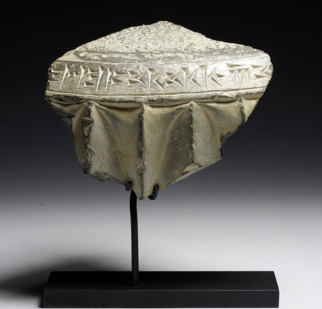 Persian Temple Fragment - Persepolis: Persepolis, Persia, ca. 550 BCE. A granite fragment of a tomb with an inscription translating to: "]…great [king], king of kings, […" Beneath inscription are deeply carved triangular shapes which