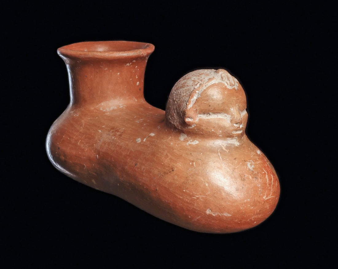Olmec Pod Effigy Vessel - Human Head & Spout, Incised Hair: Pre-Columbian, Olmec regions. Ca. 1000 - 600 BCE. Tan color pottery pod shape vessel having a wide rear spout and opposing human head, with an incised striated hairdo with a center tuft, and long narr