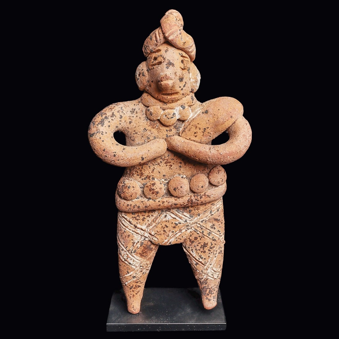 Colima Autlan Pottery Standing Lord, Gingerbread Type: Colima. Ca. 100 BCE - 250 CE. Solid pottery gingerbread type standing lord, holding both hands to his chest. Wearing a fancy decorated belt and necklace, pants incised with a crosshatched design, high