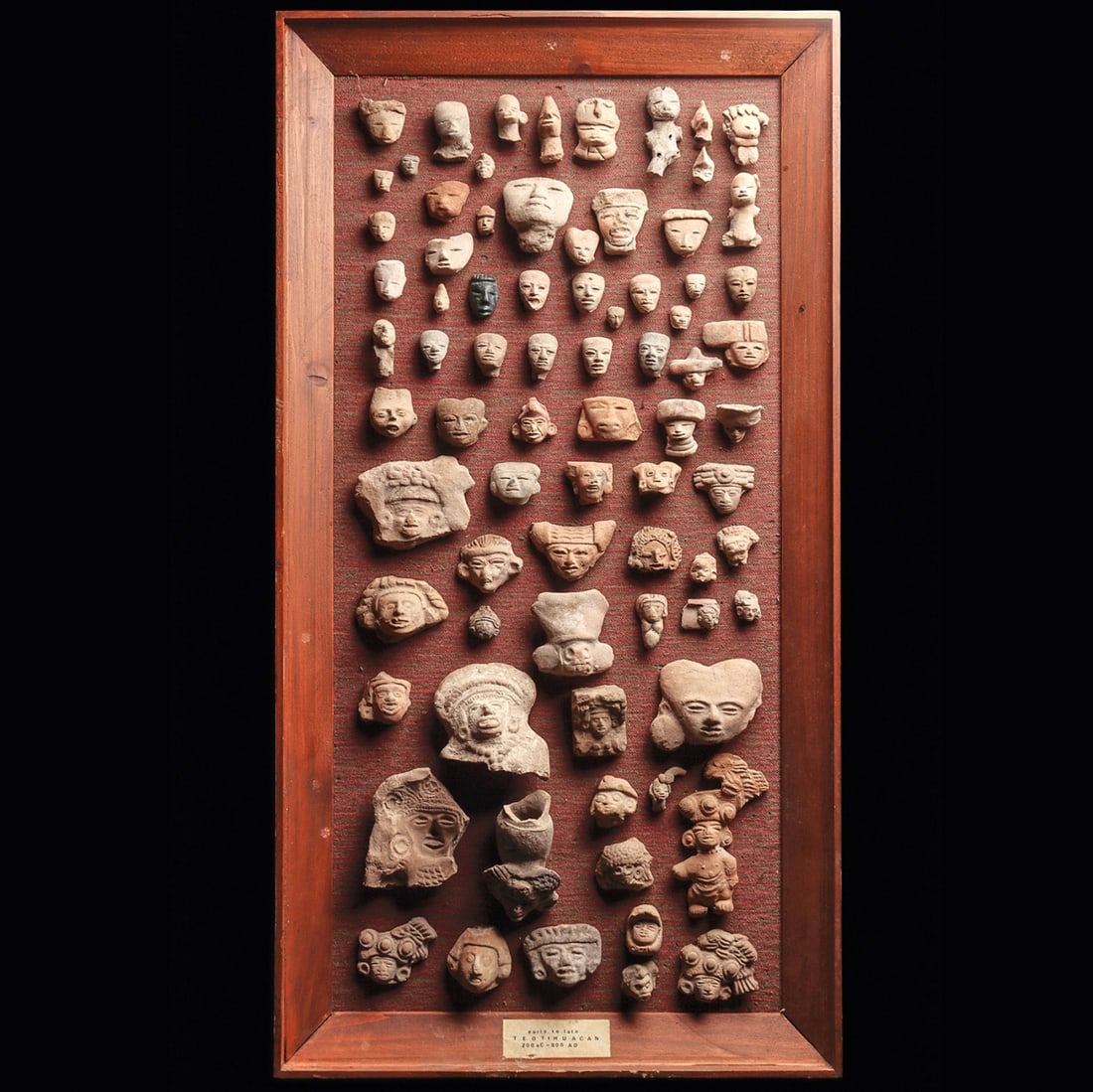 Teotihuacan Pottery Heads in Frame (75): Teotihuacan. Ca. 200 - 800 CE. Group of seventy-five pottery heads, originally from figures, and a facial mold fragment, a dark gray stone head pendant, and one figure. Some with losses and minor impe