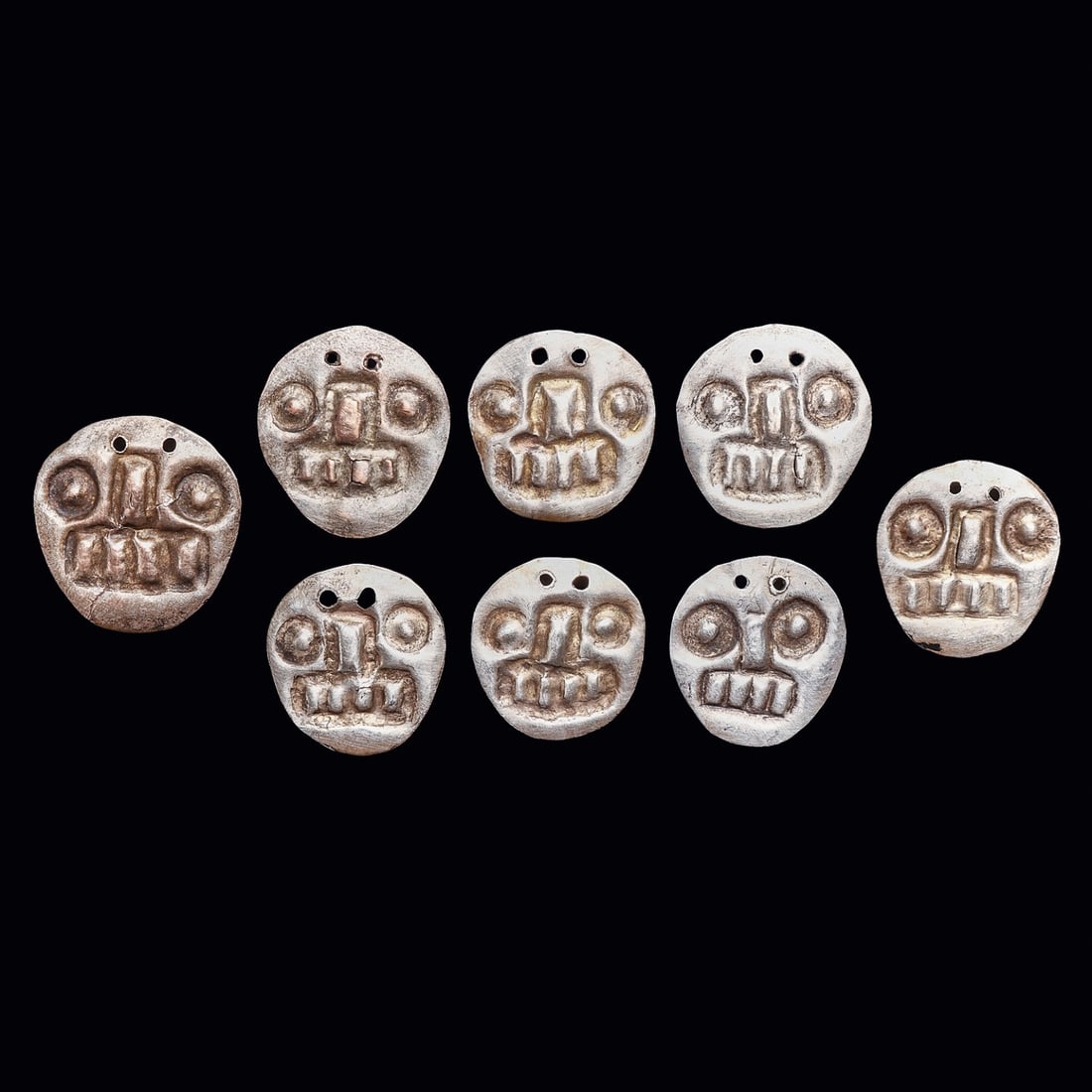 Chimu Silver Skull Dangler Attachments (8): Chimu. Ca. 1000 - 1250 CE. Eight similar sheet silver, shirt danglers, all depicting a skull face and having two attachment holes at the top. All have an excellent ancient surface patina with