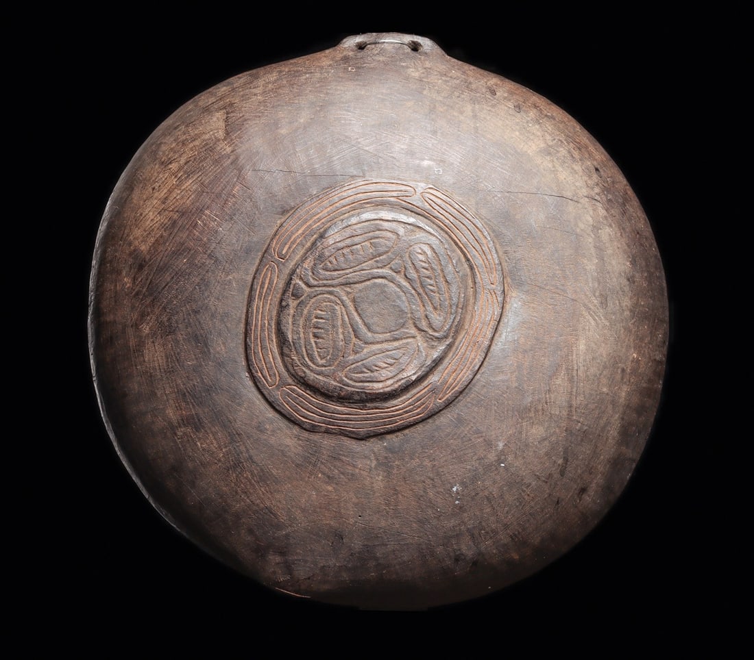 Large Boiken Vessel: East Sepik Province, Papua New Guinea. Wide shallow wood bowl carved with a raised central medallion containing an abstract motif, possibly a frog. Perforated handle on one side of rim and relief ridg